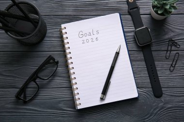 Metin Hedefleri 2026, siyah ahşap zemin üzerinde akıllı saat ve kırtasiye