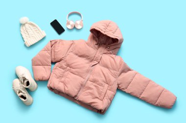 Çizmeli, kışlık şapkalı, kulaklıklı ve mavi arka planda cep telefonlu şık kısa pembe kabarık ceketli.