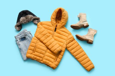 Çizmeli, kısa sarı kabarık ceketli, mavi arka planda kış şapkalı ve kot pantolonlu.