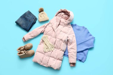 Mavi arka planda çizmeleri, kazağı, kotu ve kış aksesuarları olan şık pembe bir kabarık ceket.