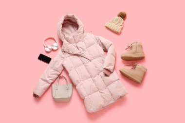 Botları, cep telefonu, kulaklıkları ve pembe arka planda çantası olan şık bir kabarık ceket.