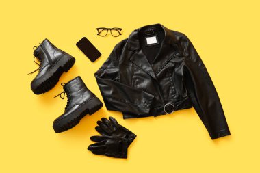 Sarı arka planda çizmeli, gözlüklü, eldivenli ve cep telefonlu şık siyah deri ceket.