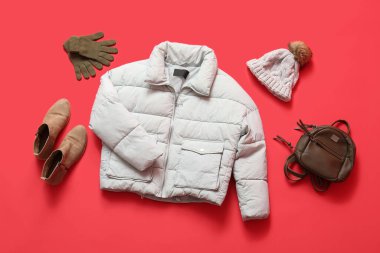 Çizmeli, sırt çantalı, kış şapkalı ve kırmızı arka planda eldivenli şık kısa gri kabarık ceket.