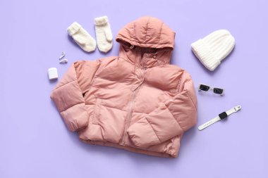 Kış aksesuarları, güneş gözlükleri, akıllı kulaklıkları ve mor arka planda kulaklıkları olan şık kısa pembe bir kabarık ceket.