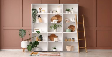 Mutfak gereçleri, bitkiler ve merdiveni olan raf odası kahverengi duvarın yanında.