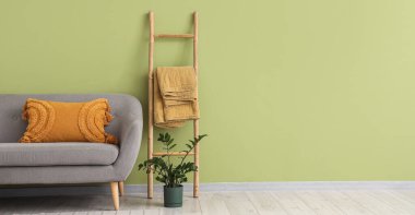 Yeşil duvarın yanında rahat gri kanepe, merdiven ve çiçek olan oturma odasının içinde.