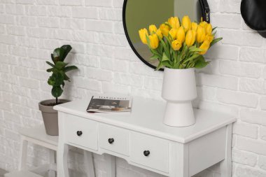 Sarı lale vazosu, aynalı ve koridordaki beyaz tuğlalı duvarın yanında saksı çiçekli.