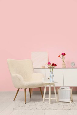 Koltuk, çekmeceler ve kahve masası. Oturma odasının içindeki vazoda Gerbera çiçekleri var.