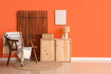 Oturma odasının iç tarafındaki turuncu duvarın yanındaki sandalye, dolap ve katlanan ekran.