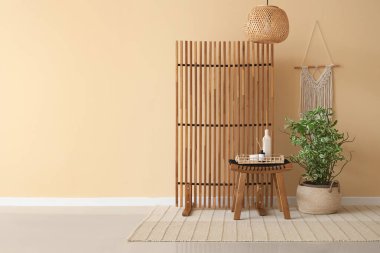 Odanın içinde bej duvarın yanındaki ahşap katlı ekran, masa ve çiçek.