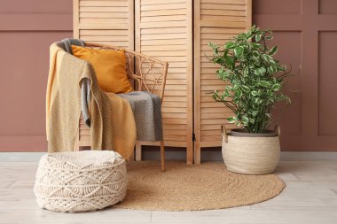 Katlanan ekran, koltuk, puf ve saksı kahverengi duvarın yanında, yakın plan.