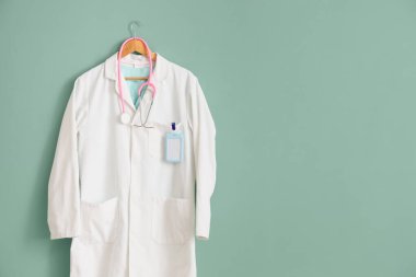 Beyaz üniformalı, rozetli ve turkuaz arka planda steteskoplu.