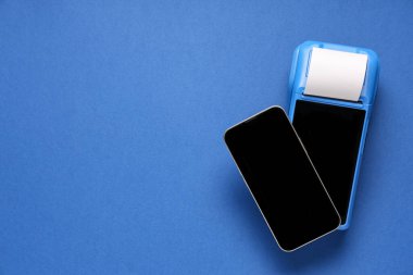 Mavi arka planda faturası ve cep telefonu olan ödeme terminali