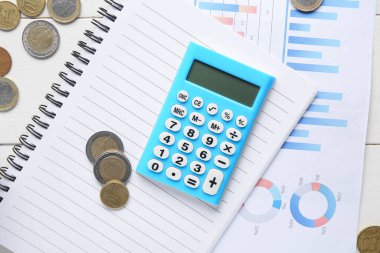 Bozuk paralar, diyagramlar ve beyaz ahşap arka planda not defteri olan hesap makinesi. Vergi ödemesi kavramı