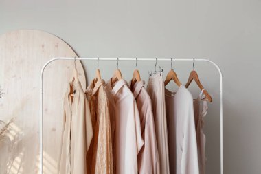 Rack with stylish female clothes near light wall