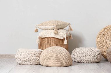 Gri duvarın yanında yumuşak yastıklar olan farklı tarz puflar ve hasır masa.