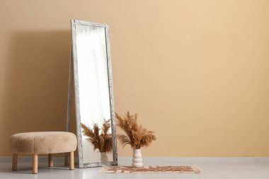 Ayna ve puf, odanın içindeki bej duvarın yanında.