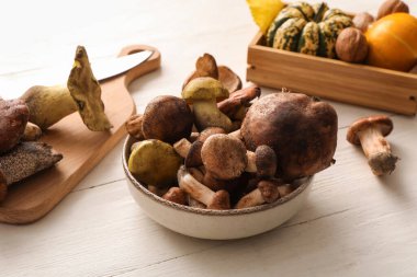 Beyaz ahşap arka planda farklı taze mantarlı kase, yakın plan.