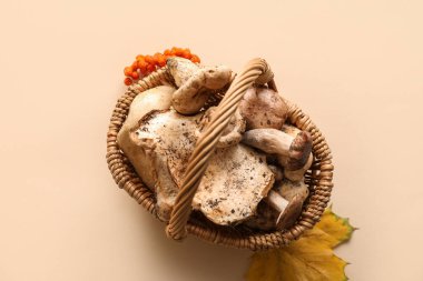 Wicker basket with fresh mushrooms on beige background, closeup