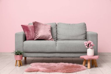 Oturma odasının içinde rahat bir kanepe, çiçek ve pembe duvarın yanındaki çiçekli vazo.