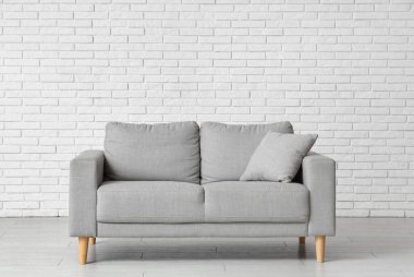 Comfortable grey sofa near white brick wall in interior of living room