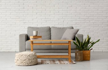 Interior of living room with grey comfortable sofa, pouf, houseplant and table