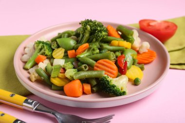 Plate with stewed mixed vegetables and fork on pink background