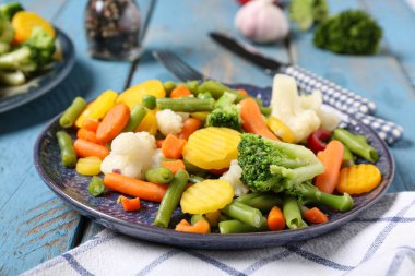 Mavi ahşap arka planda haşlanmış karışık sebzeli tabak.