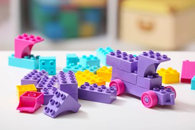 Çocuk odasındaki beyaz masanın üzerindeki renkli plastik yapı taşlarından yapılmış oyuncak araba.