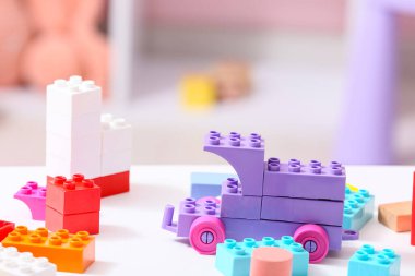 Çocuk odasındaki beyaz masanın üzerindeki renkli plastik yapı taşlarından yapılmış oyuncak araba.