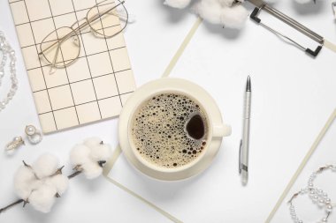 Clipboard with cup of coffee, cotton flowers, eyeglasses and jewelry on white background