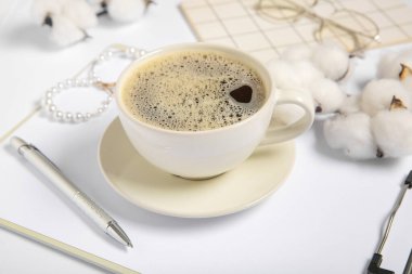 Clipboard with cup of coffee, cotton flowers and jewelry on white background