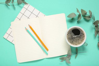Cup of coffee with notebooks, pencils and eucalyptus branches on turquoise background