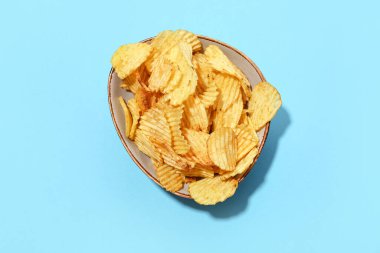 Bowl with delicious potato chips on blue background