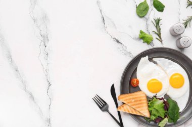 Plate with tasty fried eggs, salad mix, rosemary and toasts on marble background