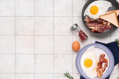 Plate and frying pan with tasty eggs, bacon, toasts, rosemary and spices on white tile background