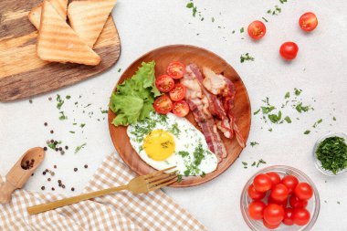 Plate with tasty fried egg, tomatoes, lettuce, bacon, dill and toasts on light background