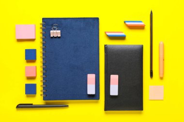 Notebooks with stationery and different rubber erasers on yellow background