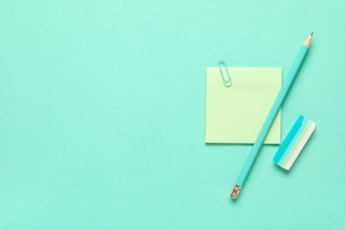Rubber eraser with sticky note, paper clip and pencil on turquoise background