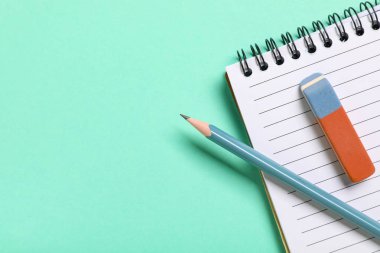 Rubber eraser with notebook and pencil on turquoise background, closeup