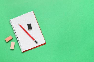 Different rubber erasers with notebook and pencil on green background