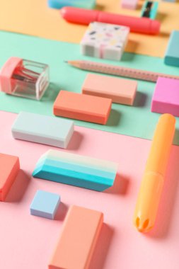 Different rubber erasers with pencil, sharpener and marker on color background