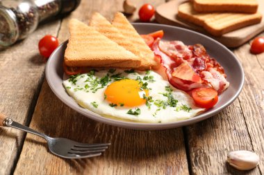 Plate with tasty fried egg, bacon, tomatoes and toasts on wooden background