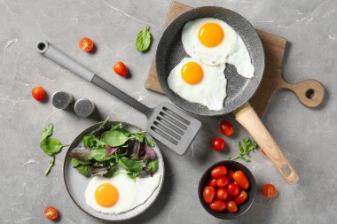 Frying pan and plate with tasty fried eggs, salad mix, tomatoes on grey grunge background