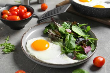 Plate with tasty fried egg, salad mix and tomatoes on grey grunge background