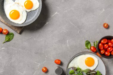 Frying pan and plate with tasty fried eggs, salad mix, tomatoes on grey grunge background