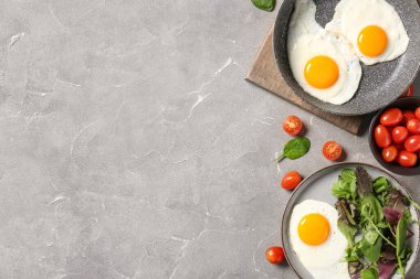 Frying pan and plate with tasty fried eggs, salad mix, tomatoes on grey grunge background