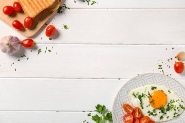 Plate with tasty fried egg, parsley, tomatoes, garlic and toasts on white wooden background