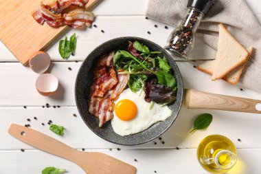 Frying pan with tasty fried egg, salad mix, bacon and toasts on white wooden background