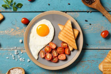 Plate with tasty fried egg, tomatoes, parsley, sea salt and toasts on wooden background